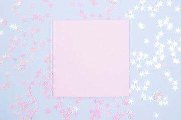 Frame of glitter stars with pink blank card mockup on blue background. Flat lay.