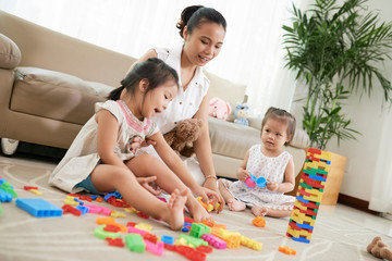 Obraz premium Happy Vietnamese mother and children making tower out of colored bricks