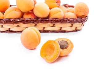 Several of harvested apricots in basket with whole and halved apricots on white background..