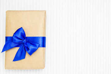 Gift in craft paper with blue ribbon and bow-knot on a white with gray line background.