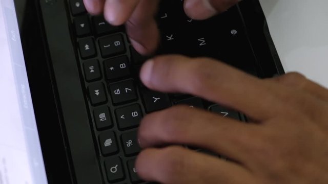Close up of brown Indian hands typing on a qwerty keyboard of a touch screen tablet 
