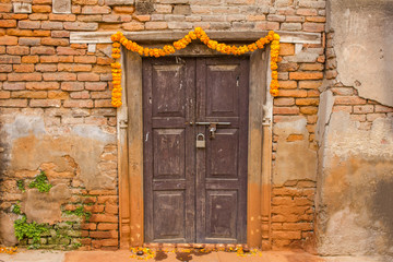 an old brown wooden door with a padlock in a damaged red brick wall, decorated with a garland of flowers for Diwali