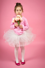 cute little girl in white tulle skirt with a bouquet of flowers on a pink background