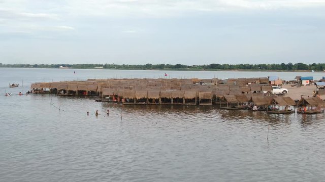 Aerial drone view fly over many parallel rows of thatched holiday huts for holiday makers and day trippers visiting the beach on a large island in the Mekong river