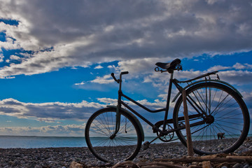 Fototapeta premium Classic (old) bicycle by the sea, blue sky with clouds, contrasting silhouette of a bicycle