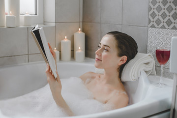 Young woman relaxes in a hot bath full of foam.