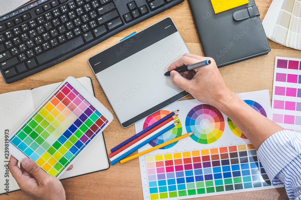 Poster Image of male creative graphic designer working on color selection and drawing on graphics tablet at workplace with work tools and accessories in workspace