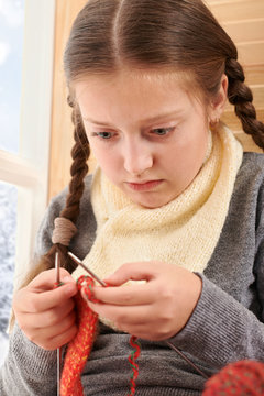 Child girl is sitting on a window sill with wool yarns and knitting. Beautiful view outside the window - sunny day in winter and snow.
