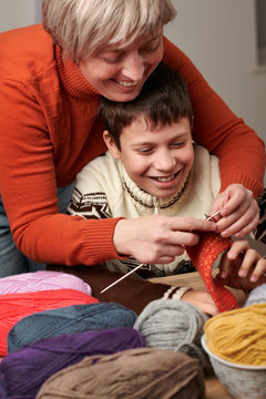 Mother is learning her child boy to knit. Colorful wool yarns are on the wooden table.