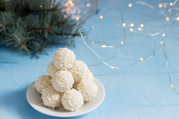 Coconut candies with white chocolate on a winter background with a garland, a candle and fir branches.