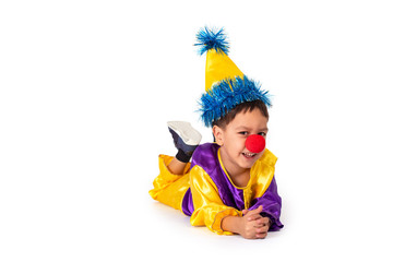 Studio shot of a little boy wearing carnival costume of a clown with a red round nose, isolate. Boy lying on the floor on his stomach