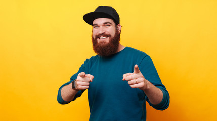 Happy smiling bearded man pointing at the camera over yellow background