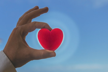 Man holding glowing red heart against blue sky . Help and donation concept.