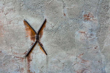Concrete wall with cracks and metal brackets in the form of a cross.