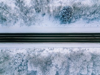 Aerial view of country road going through the beautiful snow covered landscape.