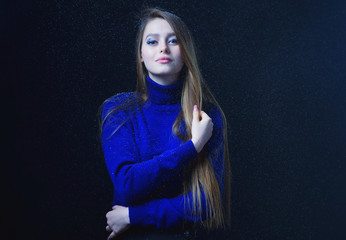 Beautiful, young girl with blond hair in a blue sweater on a snowfall in winter