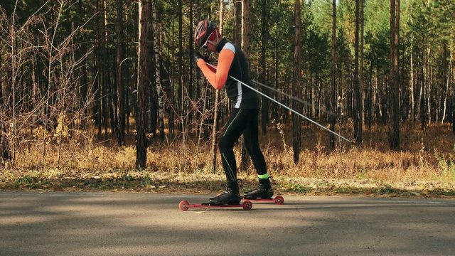Training an athlete on the roller skaters. Biathlon ride on the roller skis with ski poles, in the helmet. Autumn workout. Roller sport. Adult man riding on skates. The athlete shows the basics of