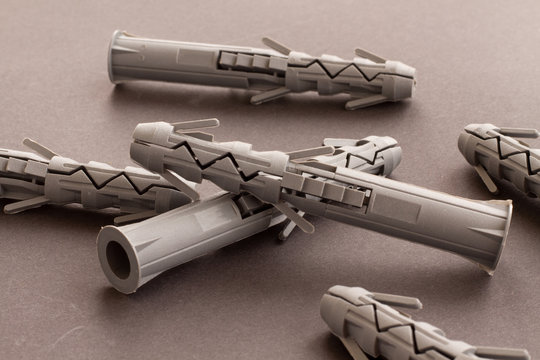 Clear pfoto of Gray plastic wall plugs and building anchors are lying on a smooth gray surface. Universal plastic mounting plugs with ribs for fast mounting wall structures.