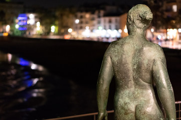 Fototapeta na wymiar Imagen nocturna de escultura de mujer desnuda de espaldas frente a playa 