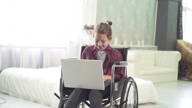 portrait of a teenage girl in a wheelchair, uses a laptop, at home in the bedroom