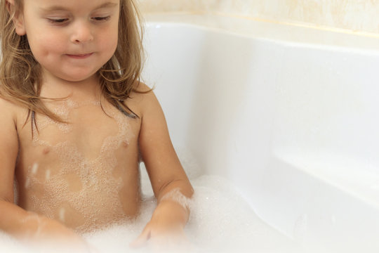 Funny baby girl splashing water playing in a bath full with foam