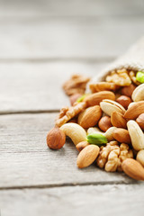 Mix of different nuts in a wooden cup against the background of fabric from burlap. Nuts as structure and background, macro. Top view.