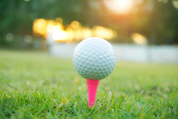 Blurred golf ball on tee in beautiful golf course at sunset background.