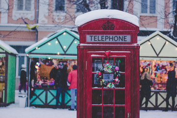 Fototapeta na wymiar red classic phone booth in winter snowing season weather time and in Christmas fair city environment