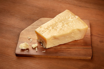A piece of aged Parmesan cheese with crumbs on a dark rustic wooden background with a place for text