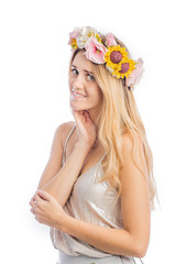 Portrait of a cute young woman in a silver blouse and a beautiful wreath of flowers on her head posing for the camera, standing in profile and holding one hand to her cheek, filming on an isolated