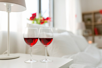 valentines day and romantic concept - two glasses of red wine on bedroom nightstand at home
