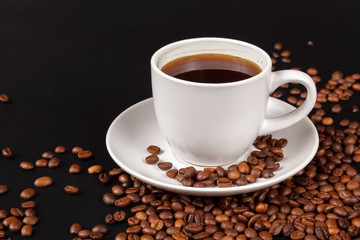 White Cup of strong coffee in roasted coffee beans, on a solid black background, foreground, close-up