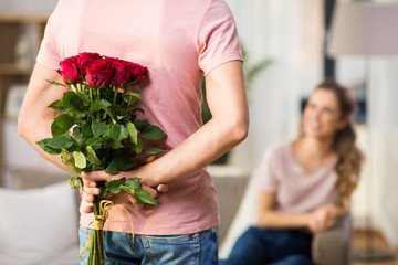 couple, relationships and people concept - happy woman looking at man hiding bunch of roses behind...