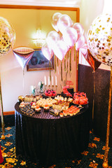 Candy bar table set. Cookies, eclairs, macaroons, fruits, cream and layered cakes. Black, golden and red colours.