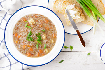 Buckwheat soup with carrot and potato on white wooden rustic table. Healthy vegetarian food, top...