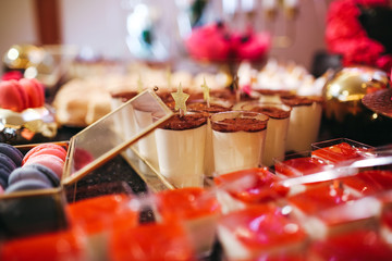 Candy bar table set. Cookies, eclairs, macaroons, fruits, cream and layered cakes. Black, golden and red colours.