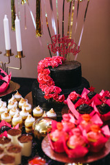 Candy bar table set. Cookies, eclairs, macaroons, fruits, cream and layered cakes. Black, golden and red colours.