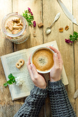A cup of cappuccino in the hands of a girl, an old wooden table, a book and cookies, instagram