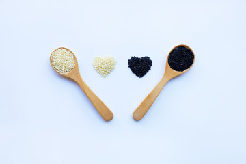Black and white sesame seeds on wooden spoon, white background.