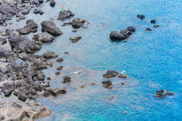 Children swim near rocky sea shore of Acitrezza, Catania, Sicily, Italy