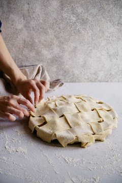 Uncooked apple pie with a wide lattice on top. Female hands making Concrete background, preparation process.