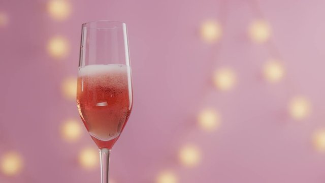 slow motion of cherry falling in glass of rose pink champagne