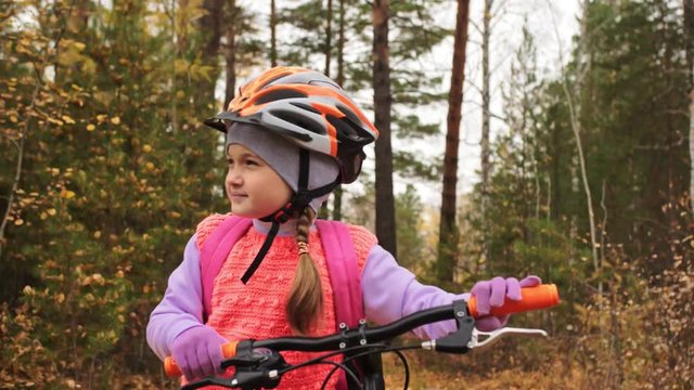One caucasian children walk with bike in autumn park. Little girl walking black orange cycle in forest. Kid goes do bicycle sports. Biker motion ride with backpack and helmet. Mountain bike hardtail.