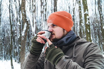 tourist man drink a hot tea, coffee in snow forest. Concept adventure active vacations outdoor. Winter camping. fleece scarf tube