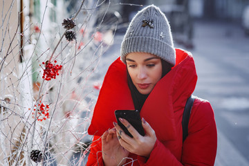 portrait of happy woman in red winter down jacket and knitted grey hat types text of sms or message...
