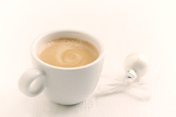 A cup of coffee and a small Christmas bauble and white wooden background. Close up. Copy space. 