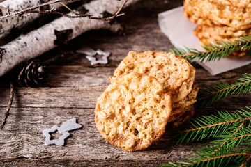 Havreflarn - scandinavian crispy slim oatmeal cookies, fir and birch branches and bark on old wooden background. Fast and easy scandinavian pastry. Cozy winter treat. Hygge. Fika. Christmas