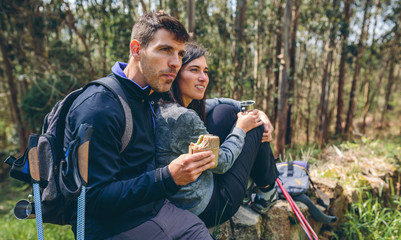 Young couple pausing to eat and drink while doing trekking outdoors enjoying nature