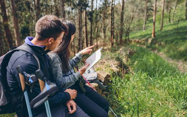 Fototapeta premium Young couple doing trekking sitting looking at a map outdoors