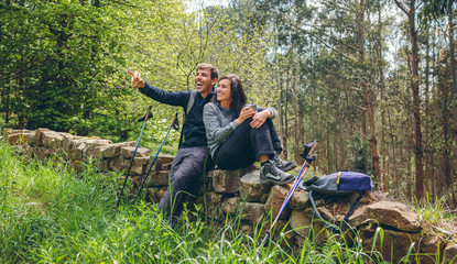 Happy young couple pausing to eat and drink while doing trekking outdoors